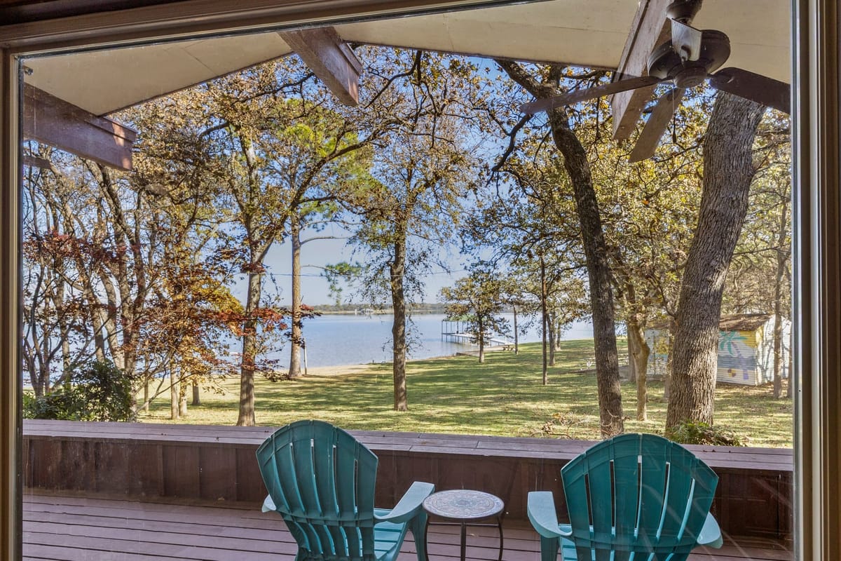 Blue Adirondack chairs on a midcentury porch overlooking the lawn and waterfront at 13030 Miller Road, an Al Komatsu-designed lake house in Azle, TX.
