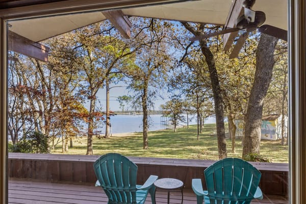 Blue Adirondack chairs on a midcentury porch overlooking the lawn and waterfront at 13030 Miller Road, an Al Komatsu-designed lake house in Azle, TX.